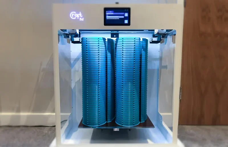 CraftBot Flow IDEX XL with dual tall blue 3D-printed towers inside, features interactive display, in a workshop setting.