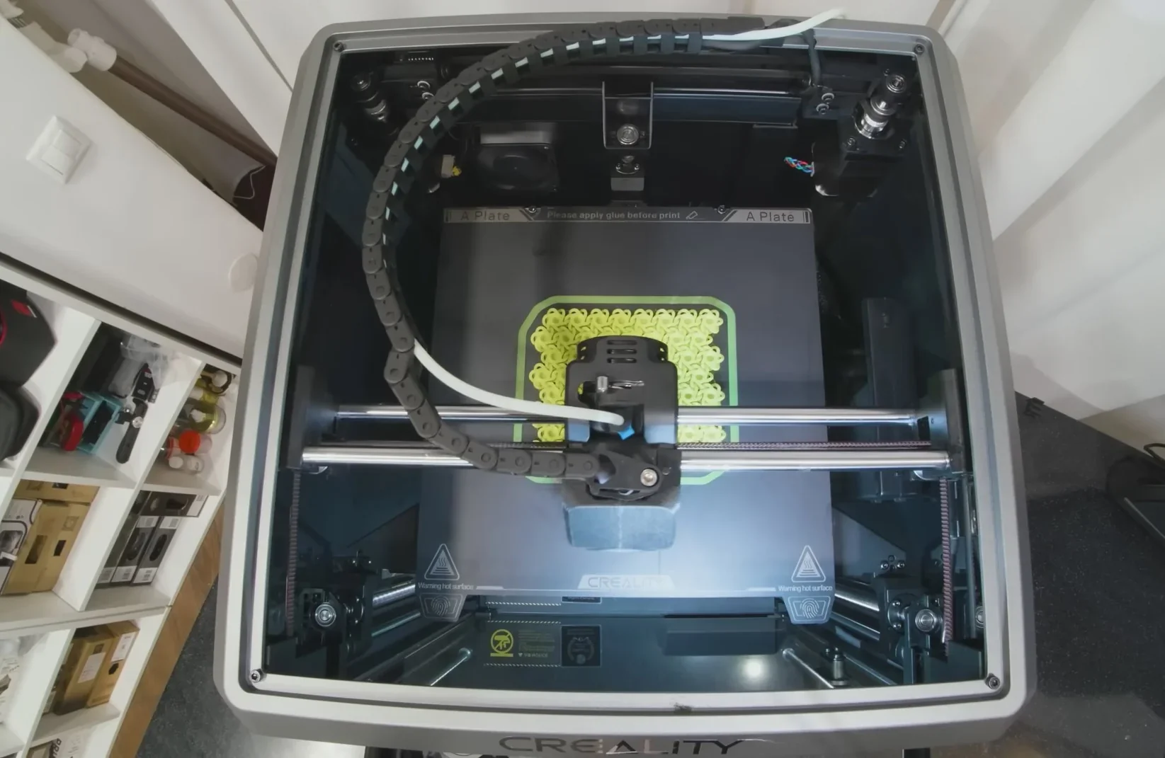 Creality K1 3D printer with yellow parts mid-print, top view showing mechanical interior, branding visible on frame.