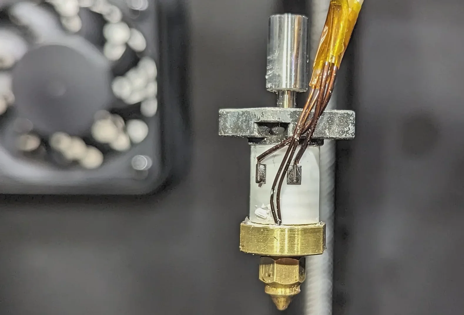 Creality K1 3D printer nozzle close-up showing metal extruder and wiring details with blurred fan in the background.