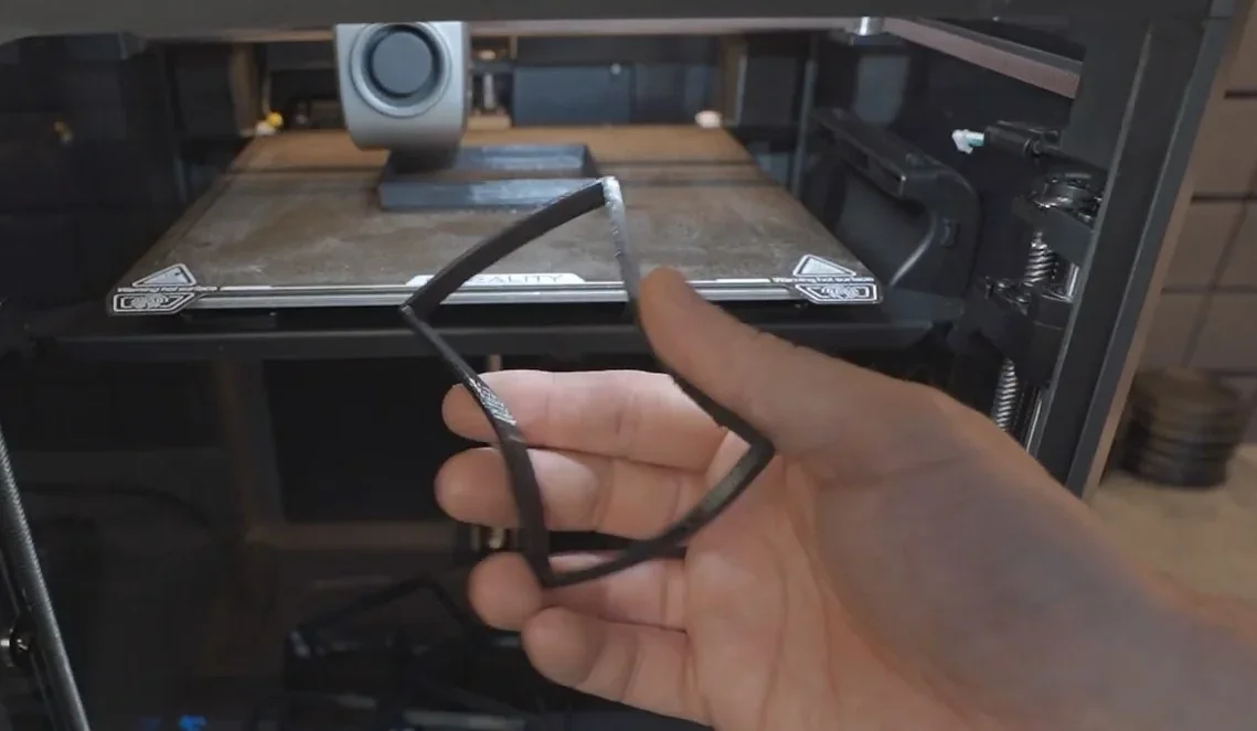 Hand holding a 3D-printed frame inside Creality K1 printer, showcasing precise craftsmanship.