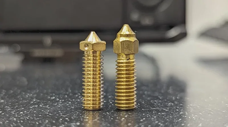 Creality K1 brass nozzles on reflective surface, showcasing threaded design and intricate detailing.