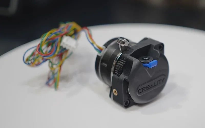 Creality K1 3D printer component with colorful wires connected, featuring branding on a circular black part against a blurred dark background.