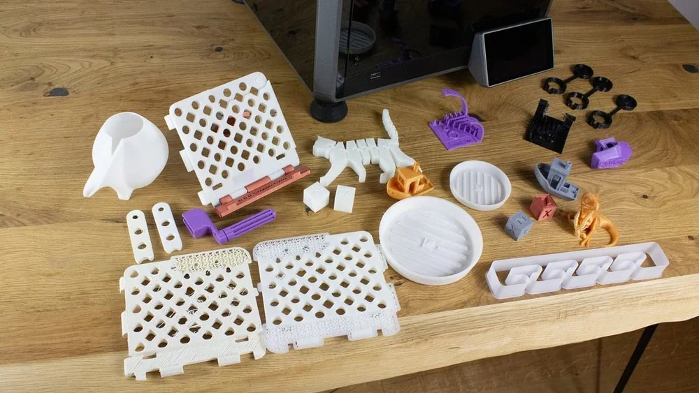 Creality K1 3D printer on a wooden table with various printed samples, including geometric shapes and functional parts, showcasing printing capability.