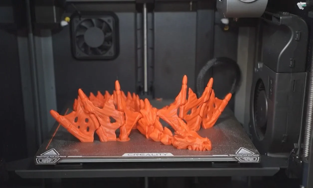 Creality K1 3D printer with an intricate orange dragon-like model on the print bed, fan and printer components visible.