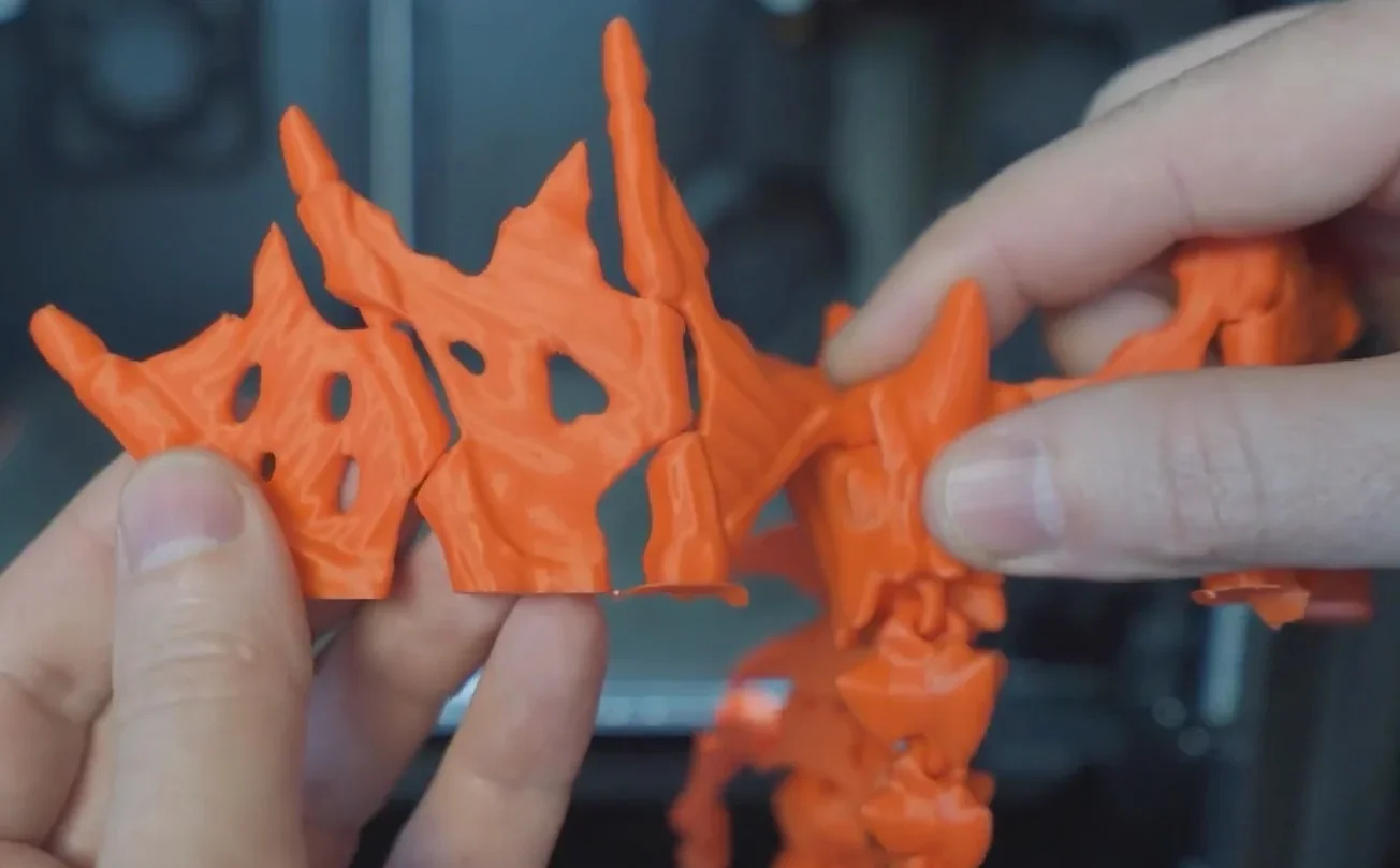 Hands holding detailed orange 3D-printed parts with jagged edges, created by Creality K1, showcasing intricate design capability.