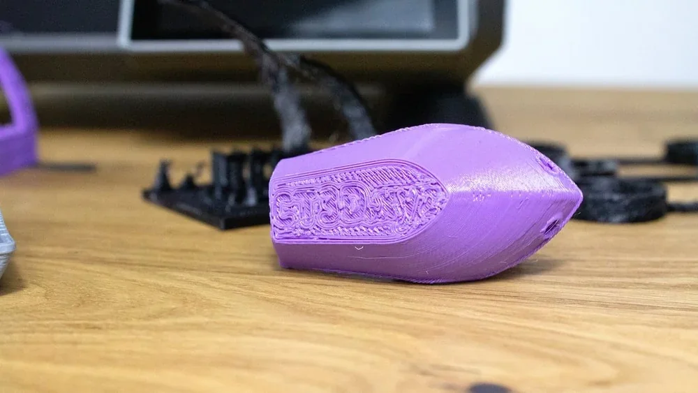 Purple 3D-printed model created by Creality K1 on a wooden table with other parts in the background.