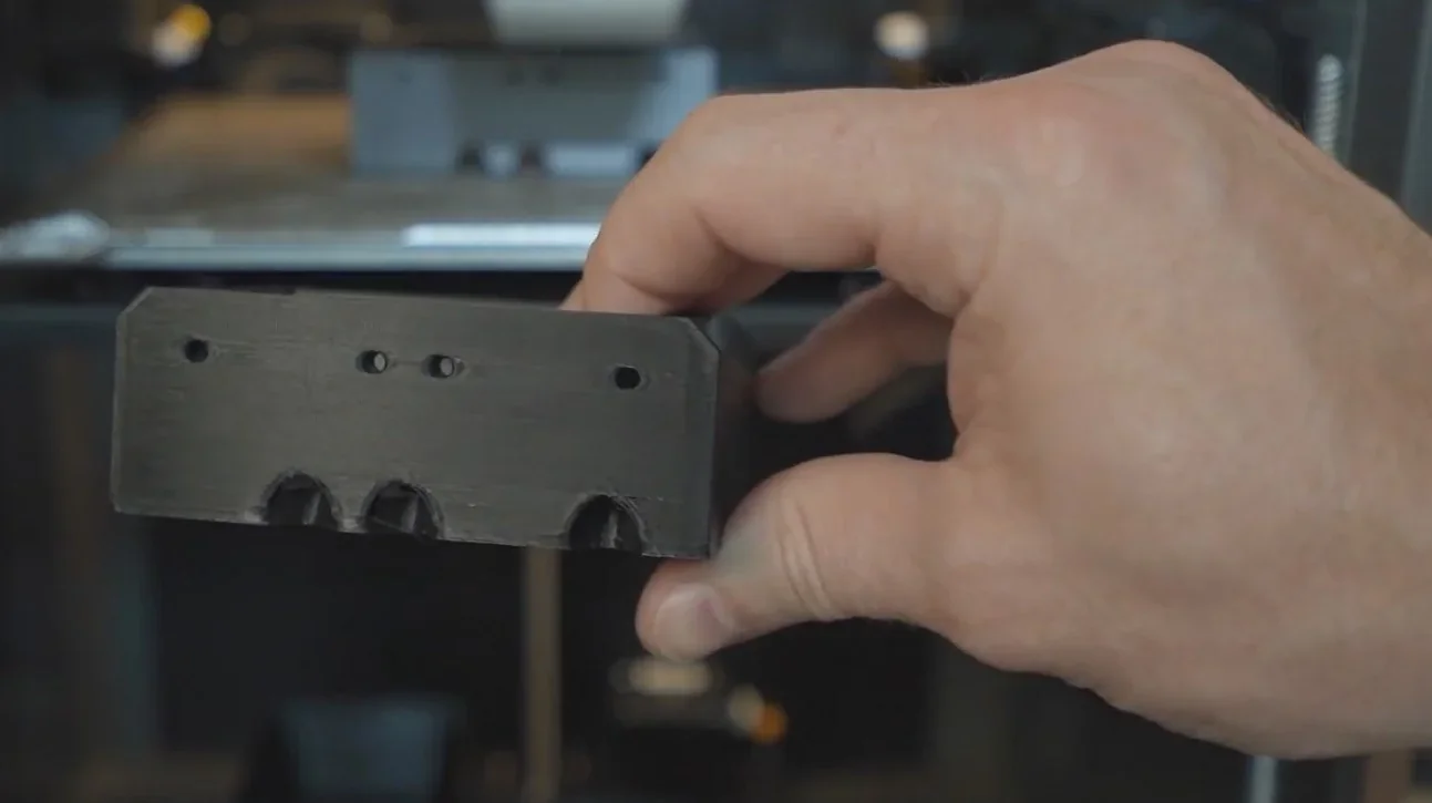 Hand holding a black 3D-printed component created by the Creality K1, highlighting intricate details, with the printer in the background.