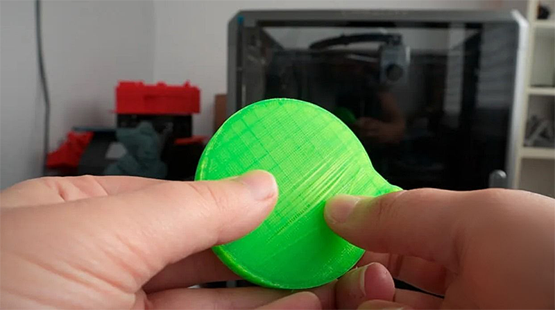 Creality K1 Max 3D printer in background, green circular 3D-printed object held in hand, showcasing print quality; indoor setting.