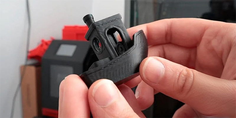 Hands holding a black 3D-printed boat created by Creality K1 Max, with the printer visible in the background.