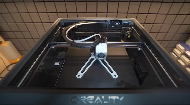 Creality K1 Max 3D printer in a tiled room with advanced extrusion system, glass top view, showing internal parts and branding on the frame.