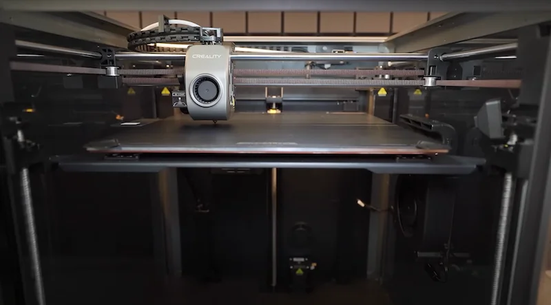 Creality K1 Max 3D printer with detailed components and visible branding, showcasing its printing bed inside an enclosed structure.