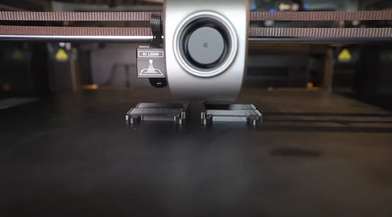 Creality K1 Max 3D printer head printing sample parts with AI lidar, in a workshop setting, showcasing precise manufacturing technology.