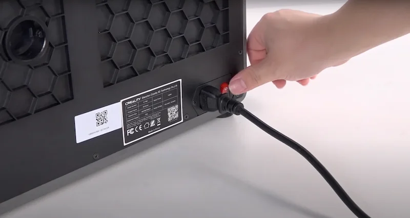 Creality K1 Max 3D printer back panel with honeycomb design, labeled ports, and power cord being plugged in by a hand for operation.