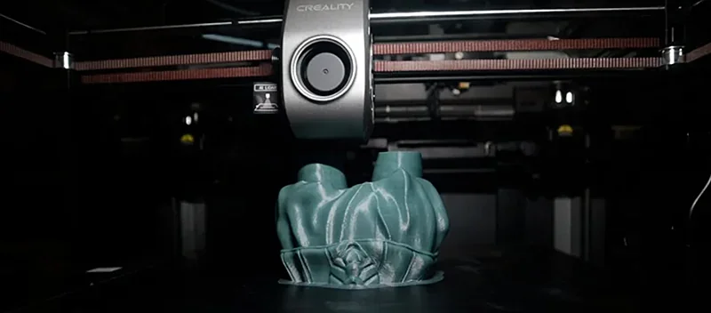 Creality K1 Max printing a detailed green 3D model, showcasing build plate and extruder in a dark setting.