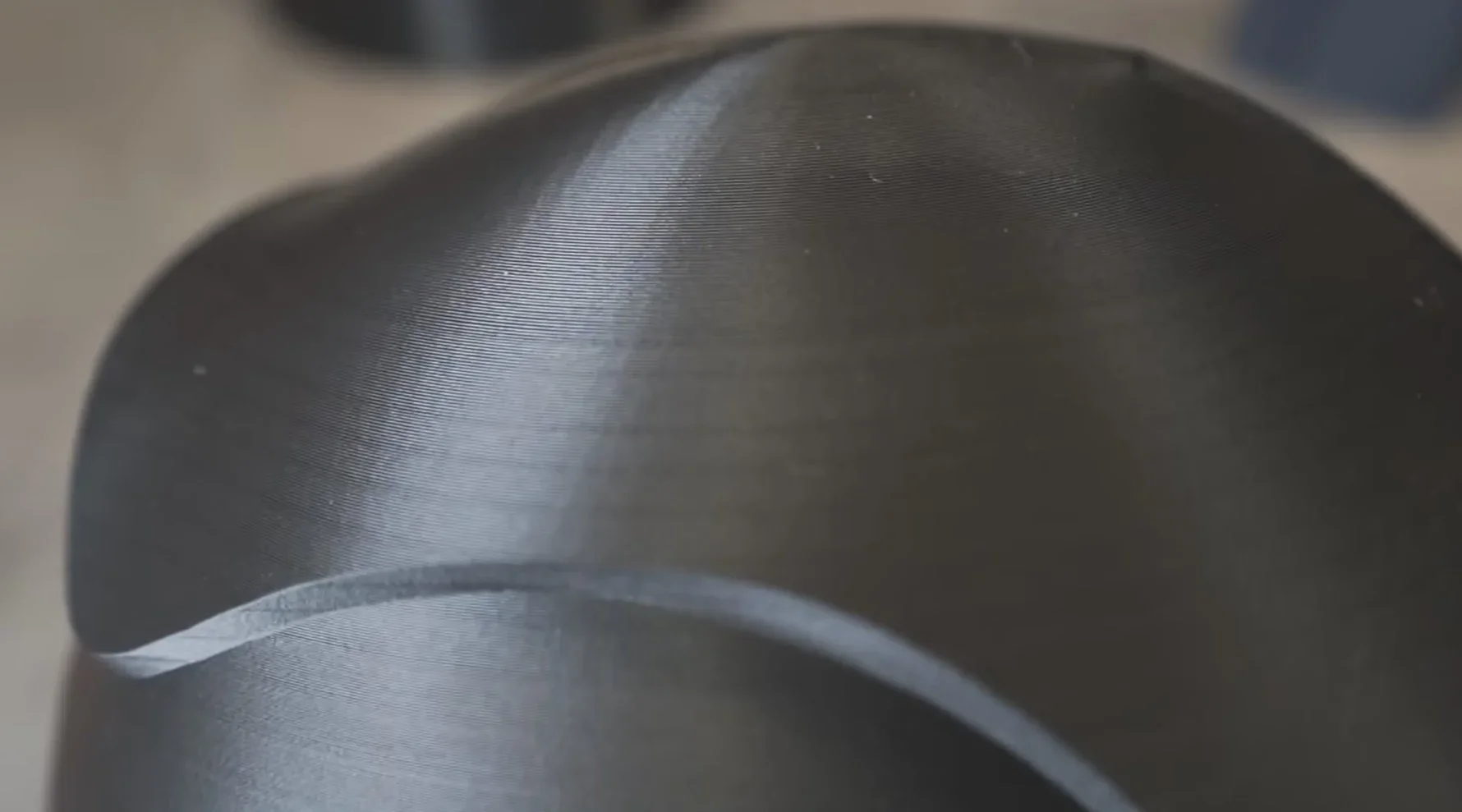 Close-up of a smooth, black 3D printed object created by Creality K2, showcasing fine layer lines and curved design details.