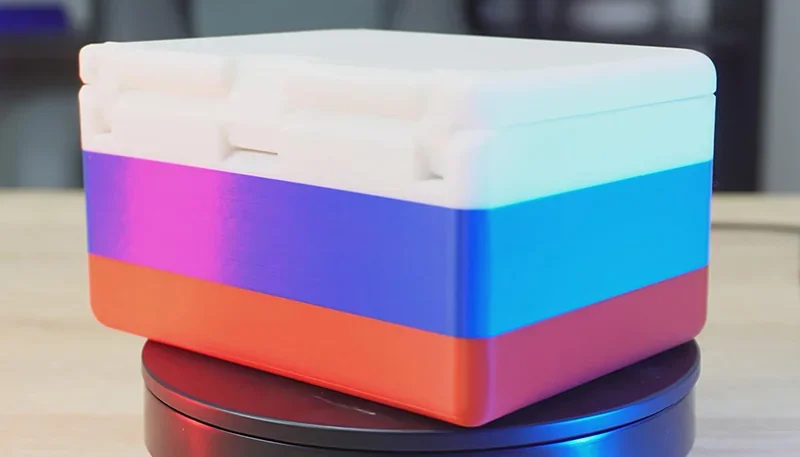 Colorful 3D-printed box with a layered design in white, purple, blue, and red, crafted by the Creality K2, displayed on a rotating platform.