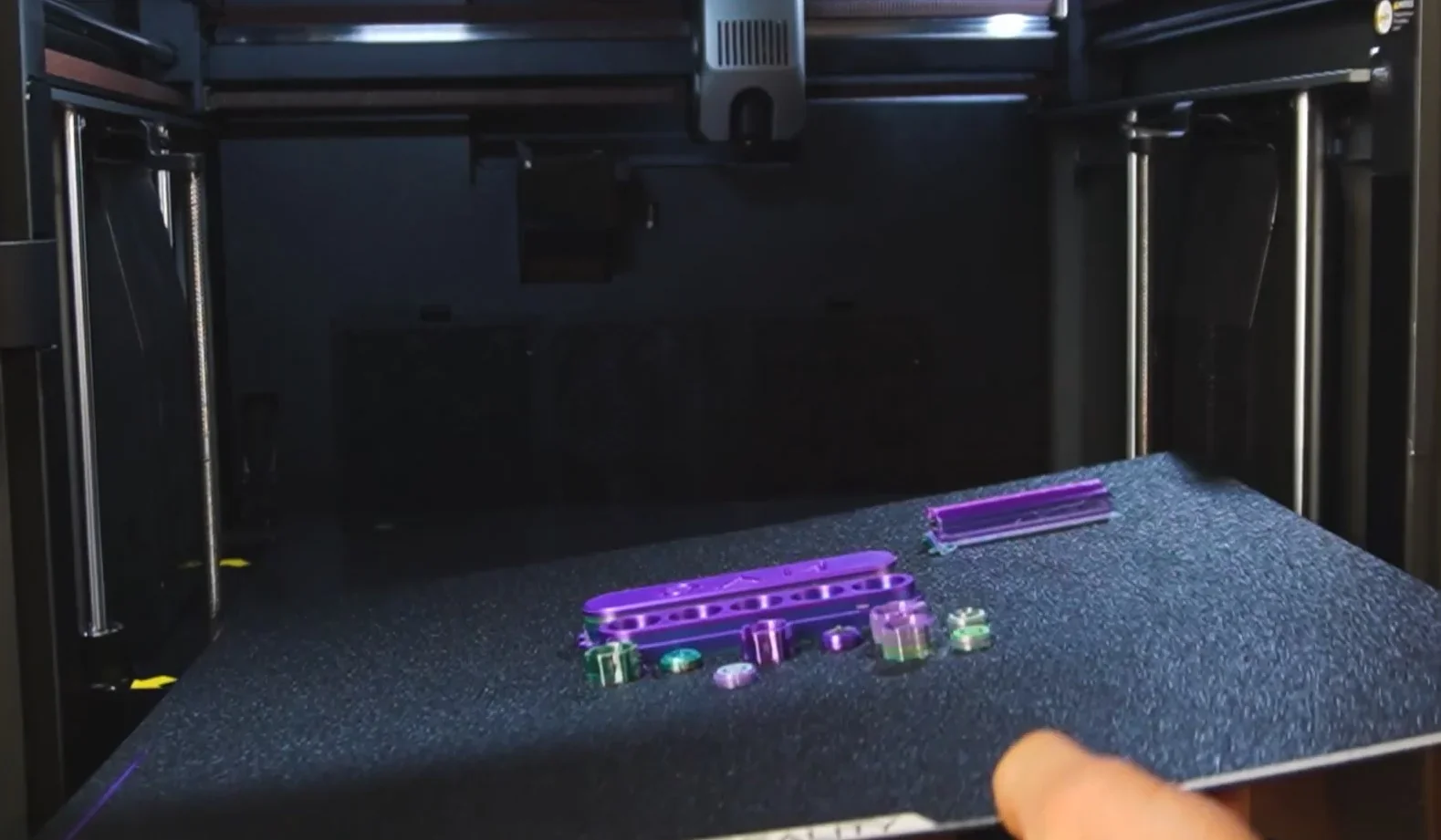 Creality K2 3D printer interior with purple and green printed parts showcased on the printing bed, displaying precision and quality.