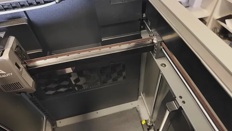 Creality K2 3D printer interior with metal rails and components; branding visible on the extruder.