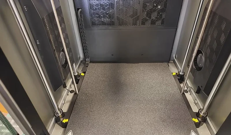 Creality K2 3D printer interior with textured printing bed, z-axis rods, and cooling vents, highlighting durable design ideal for accurate part creation.