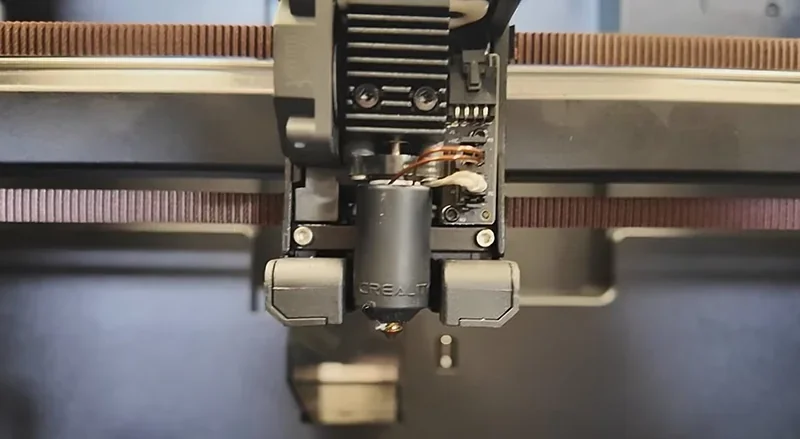 Creality K2 3D printer nozzle and extruder close-up, with visible wires and mechanical components, in a workshop setting.