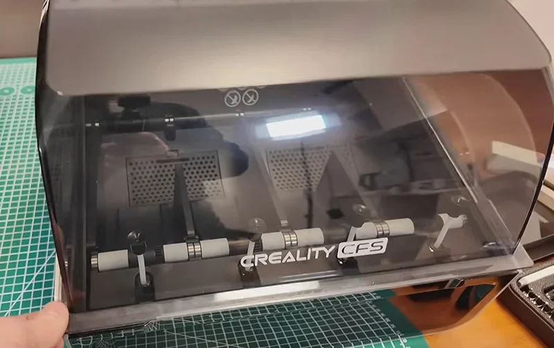 Creality K2 3D printer with transparent cover displaying internal components, placed on a green cutting mat, showcasing Creality branding.