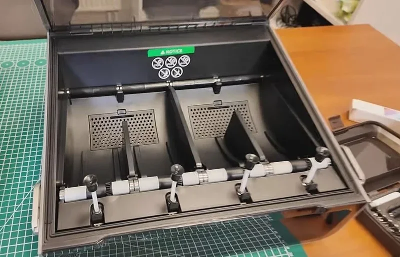 Creality K2 3D printer with open chamber showing dual compartments and rollers, set on a green cutting mat under bright lighting.