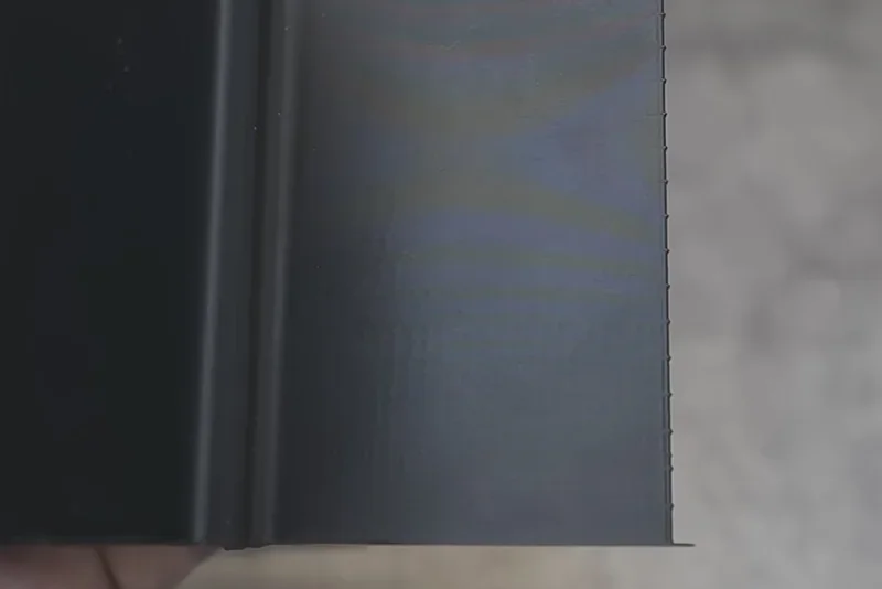 Close-up of a smooth, dark 3D-printed surface created by Creality K2, showcasing fine texture and precision in an indoor setting.