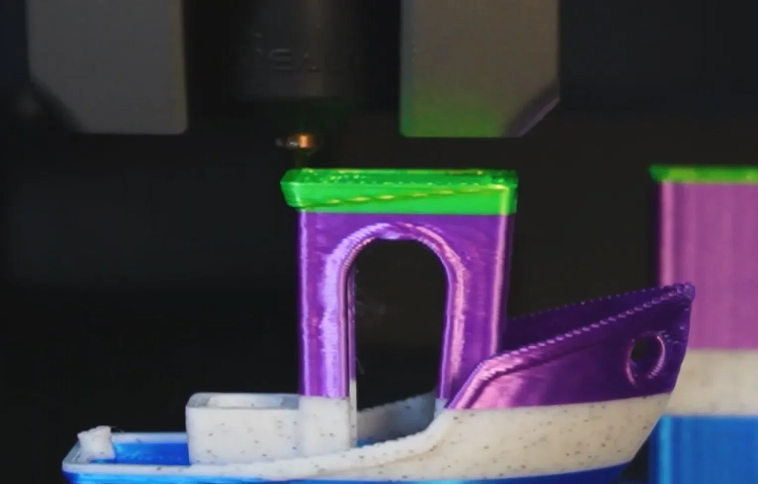Creality K2 3D printer creating a colorful boat model with green, purple, and white layers, showcasing detailed and precise extrusion.