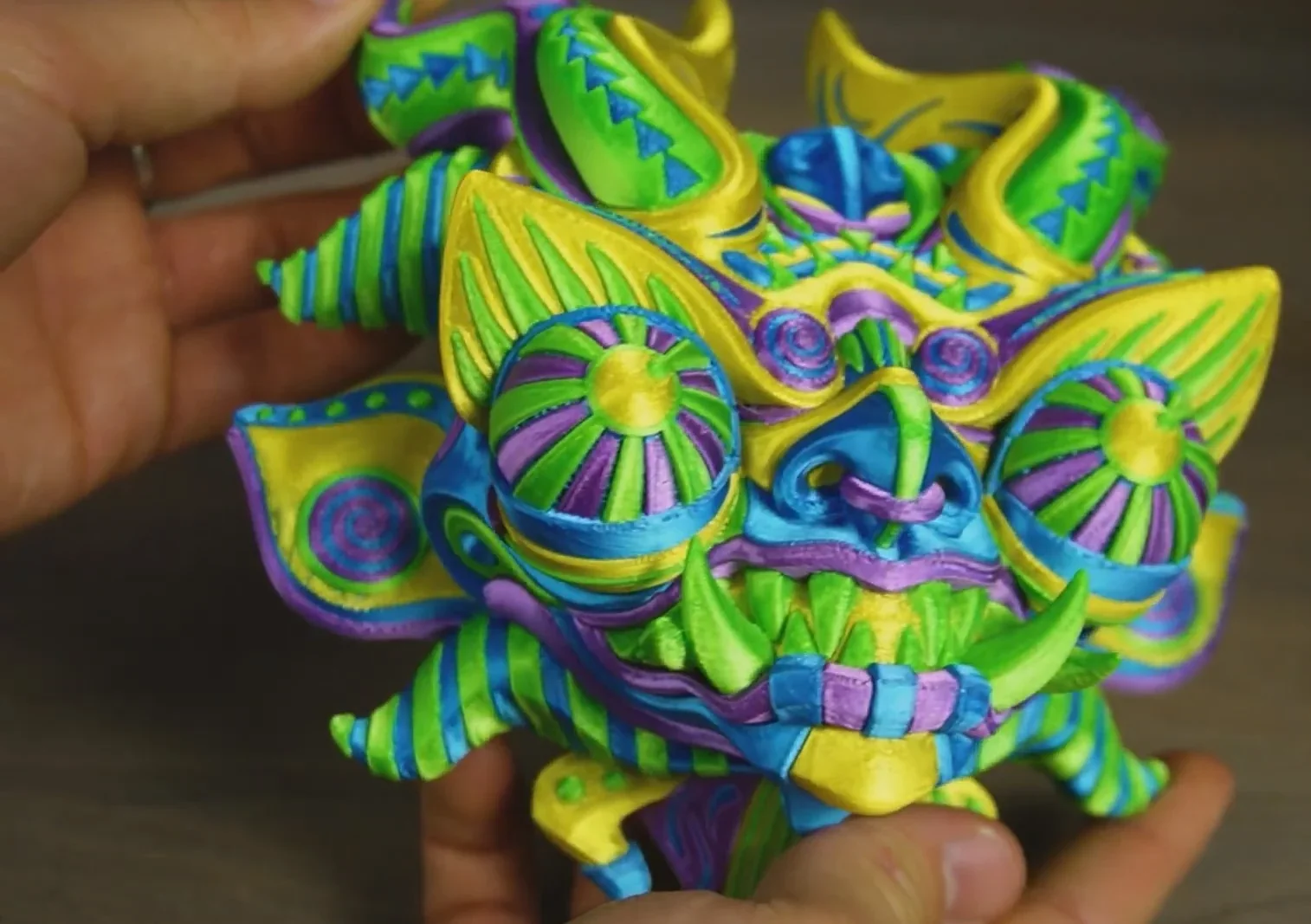 Colorful 3D-printed mask with intricate patterns, created by Creality K2. Bright greens, purples, blues, and yellows enhance the design.