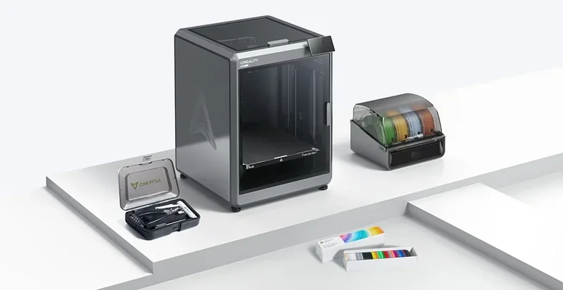 Creality K2 3D printer with transparent enclosure, filament holder, tool kit, and filament samples displayed on a white surface.