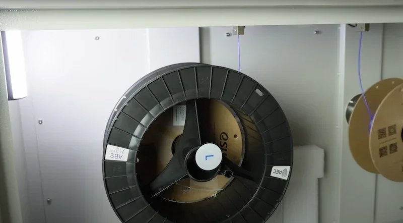 Creatbot D1000 3D printer filament spools inside the machine, showing ABS and REC labels, with filament threads aligned for printing.