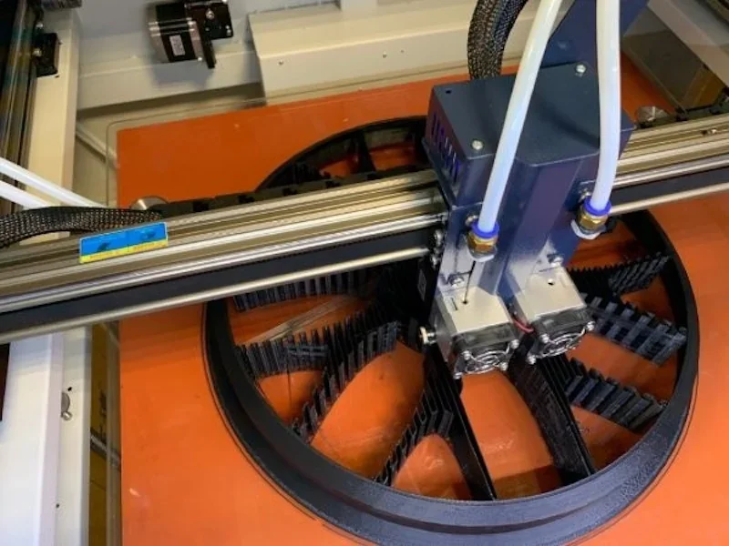 Creatbot D600 Pro printing a large, intricate black component on an orange platform, featuring dual extruders in a workspace setting.