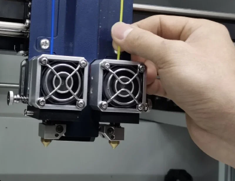 Hand adjusting dual extruders on a Creatbot D600 Pro 3D printer, showcasing the printer's precise engineering and filament handling capabilities.