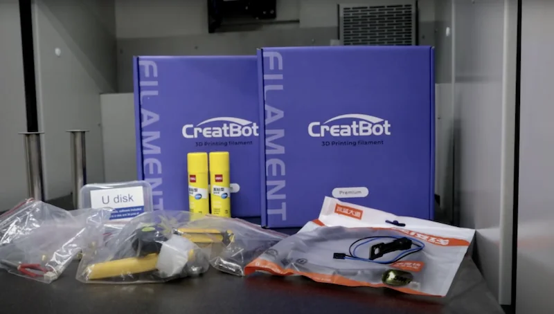 CreatBot D600 Pro2 HS supplies including filament boxes, U disk, glue sticks, and tools displayed on a table, with branded packaging visible.