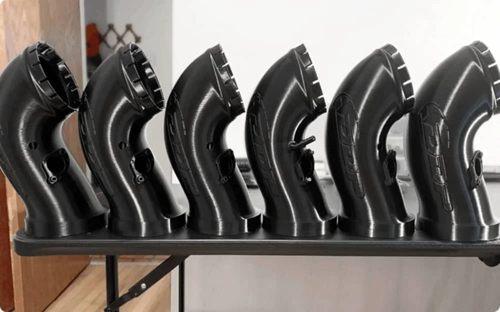 Six black, curved 3D-printed parts on a table, created by the Creatbot D600 Pro2 HS, showing detailed smooth finishes in a workshop setting.