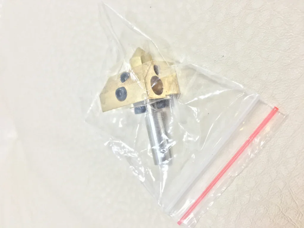 Creatbot F160 3D printer nozzle in a clear plastic bag on a light surface, showcasing its brass material and intricate design details.