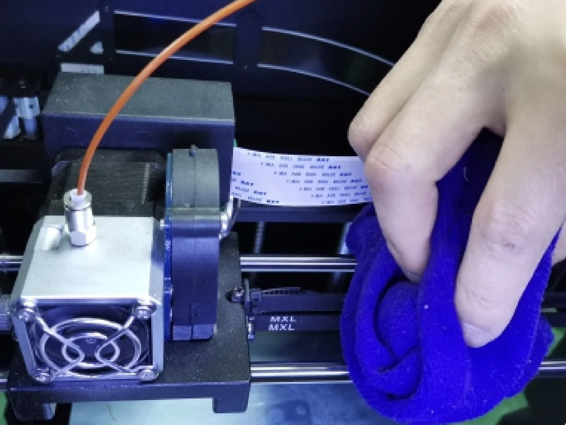 Creatbot F160 3D printer with extruder in focus; hand cleaning the print bed with a blue cloth.