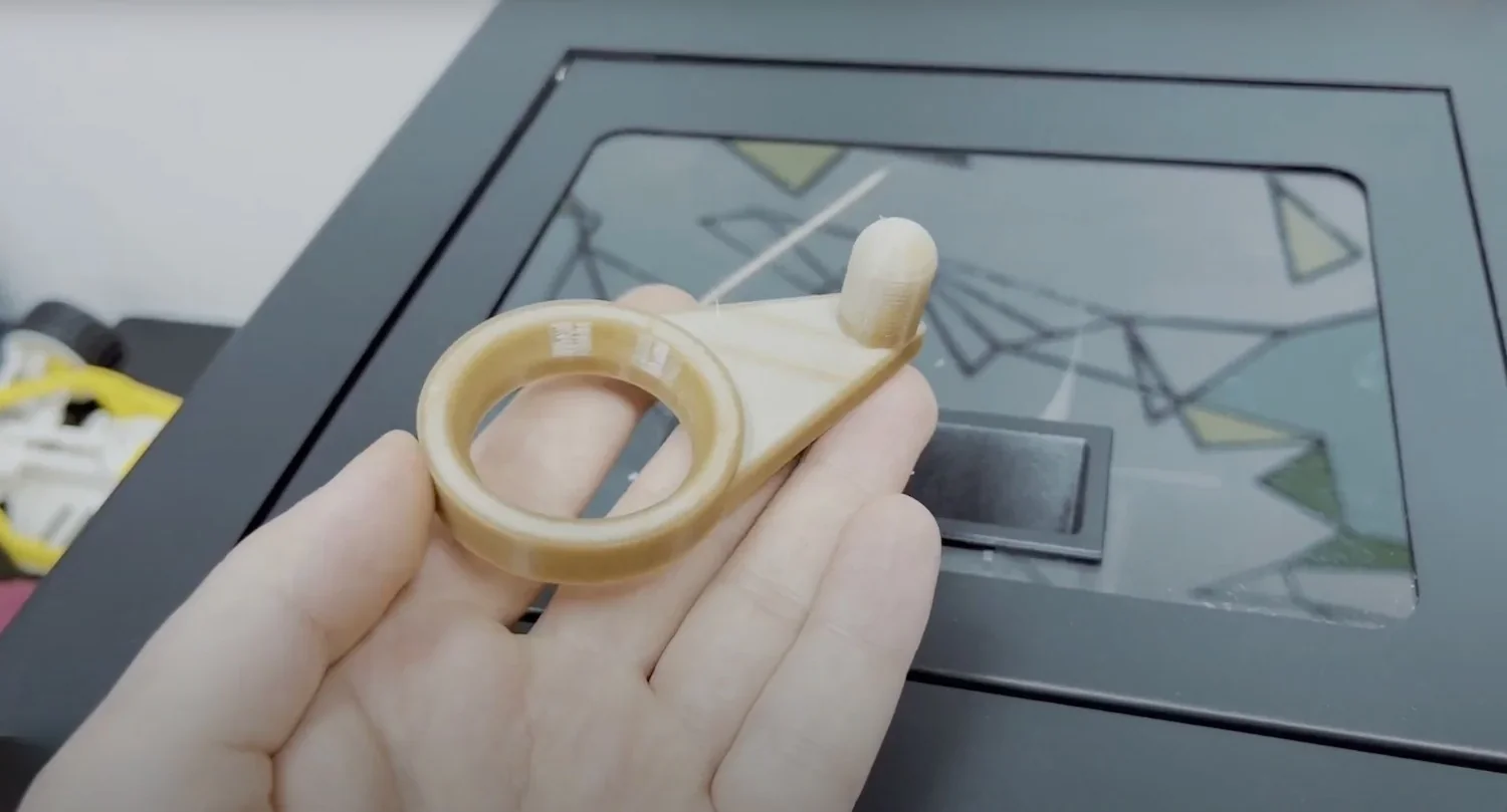 Hand holding a 3D printed beige part created by Creatbot F160, against the printer's geometric-design build plate in the background.
