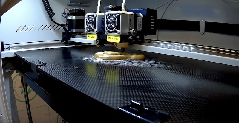 Creatbot F430 3D printer with dual extruders prints yellow filament on carbon-fiber print bed; internal setup visible, showcasing precision engineering.