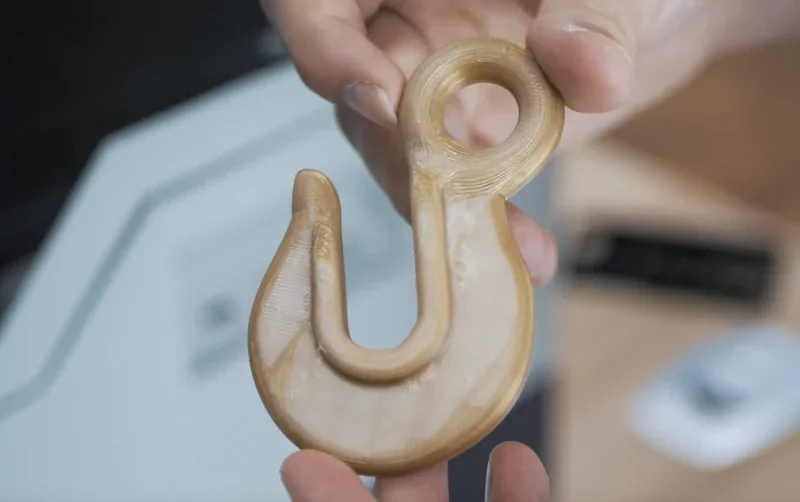 Creatbot F430 3D-printed beige hook held in hand, showcasing detailed craftsmanship and design capabilities in a tech workshop setting.