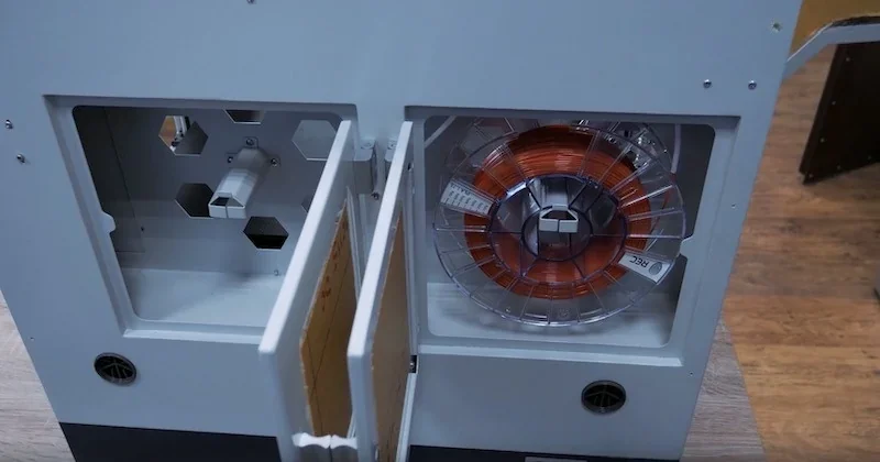 Creatbot F430 3D printer in workspace showing filament spool inside open side panel, hexagonal vent pattern visible, wooden floor background.