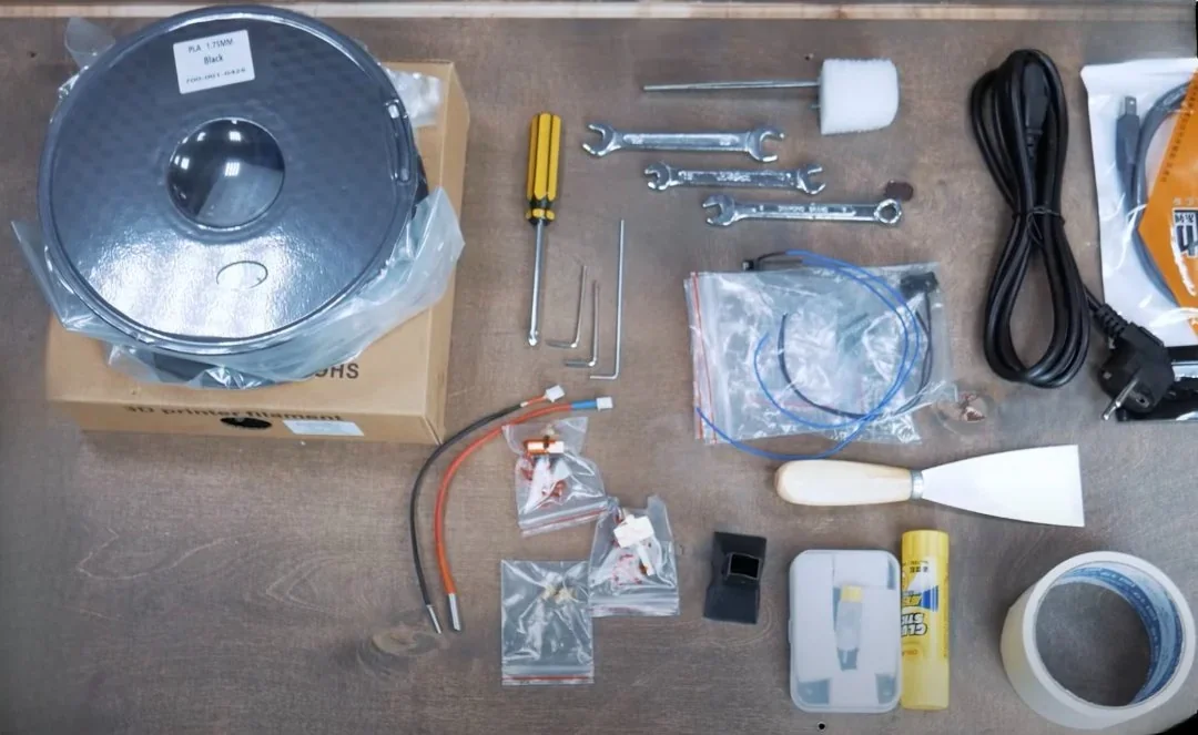 Creatbot F430 3D printer accessories: filament spool, tools, cables, glue stick, scraper, tape, and spare parts arranged on a wooden surface.