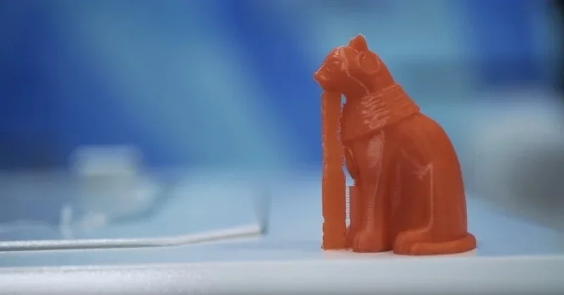 Orange cat figurine 3D printed by the Creatbot F430, on a smooth surface, against a blurred blue background.