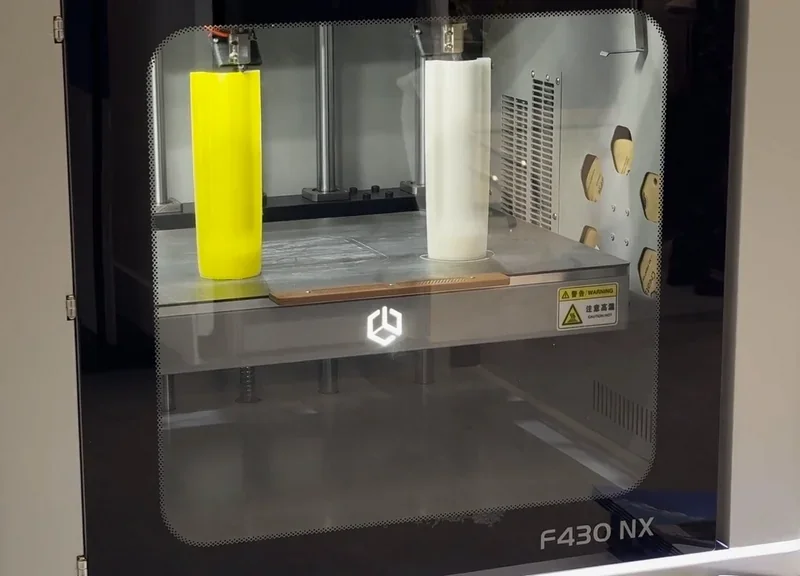 Creatbot F430 NX 3D printer with yellow and white cylindrical models inside, sleek glass door, visible branding, creating precise part samples.