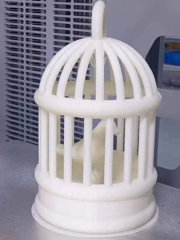 3D-printed birdcage model created by the CreatBot F430 NX, featuring vertical bars and a central bird figure in a tech environment.