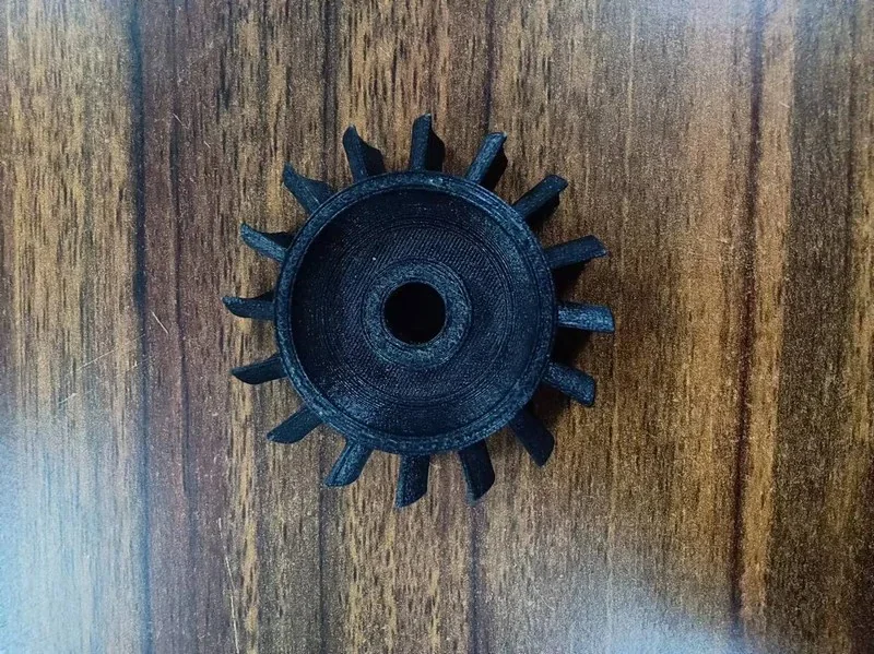Black 3D-printed gear on wood surface, showcasing fine detail and quality, created by Creatbot Peek-250.