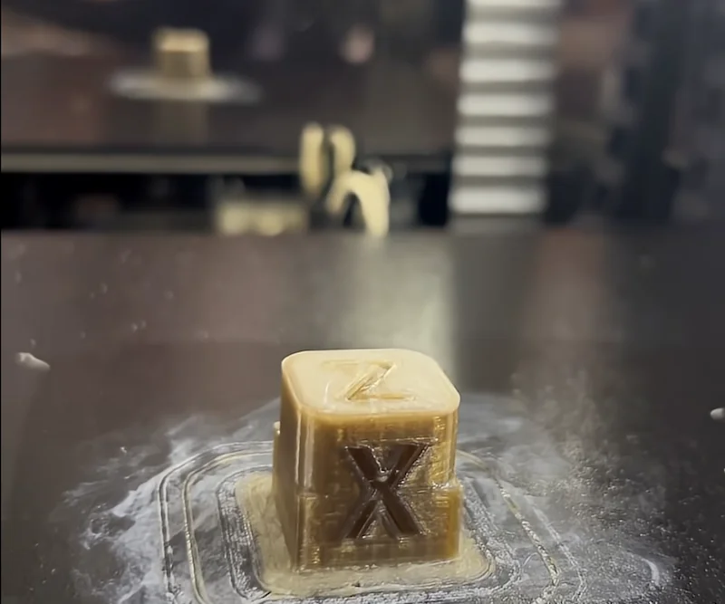 Creatbot PEEK-250 printing a small cube with engraved letters on a smooth dark surface, showcasing its precision and material capabilities.