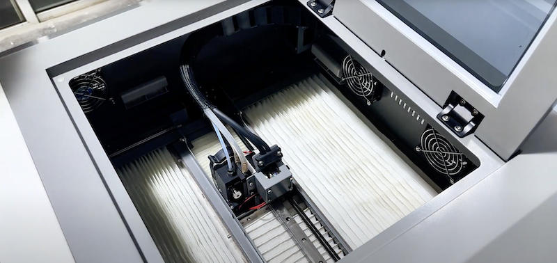 The interior of the CreatBot PEEK-250 3D printer is shown, highlighting the dual-extruder system on a guiding rail. Visible components include wiring, cooling fans, and a spacious build area, emphasizing its precise and efficient performance in a professional setting.