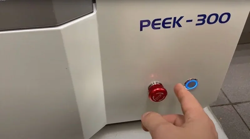 Hand interacts with Creatbot PEEK-300 3D printer, pressing red button. Device shows brand logo on sleek panel, indicating advanced tech features.