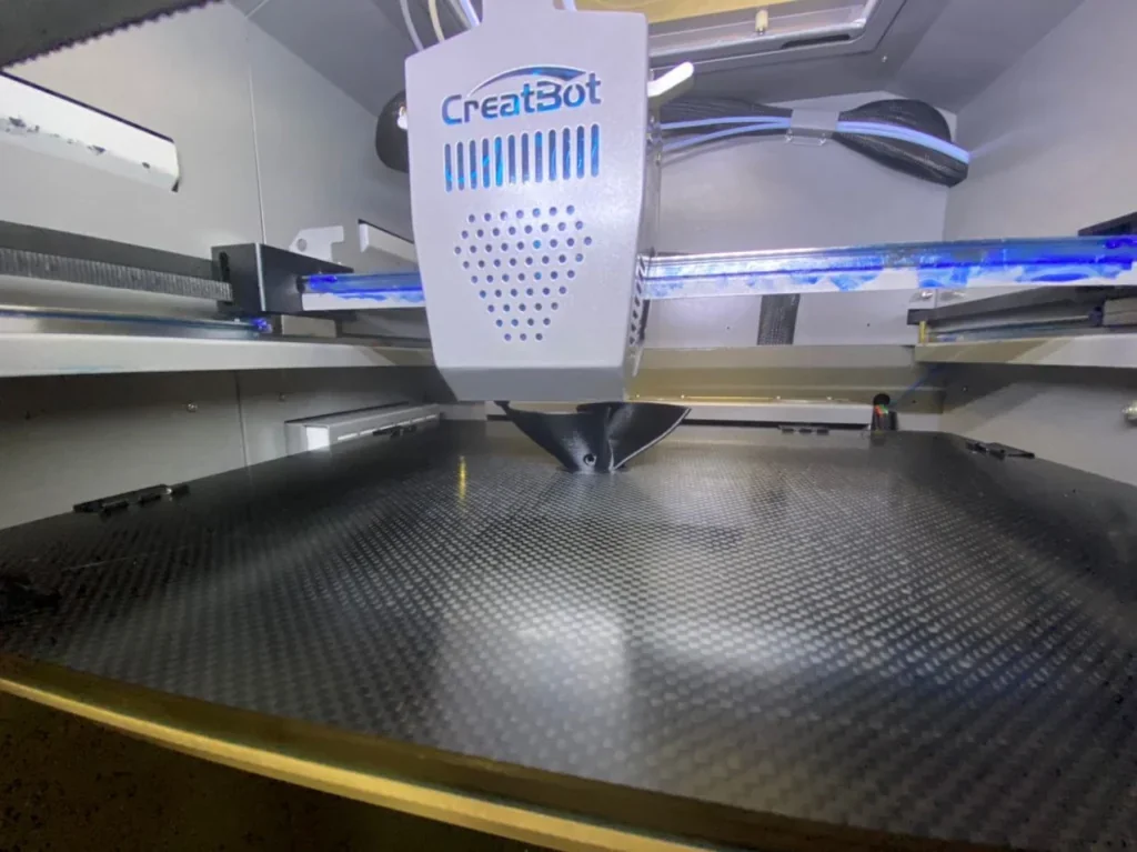 Creatbot PEEK-300 3D printer in action on a carbon print bed, showcasing precise filament work and branding in an enclosed setup.